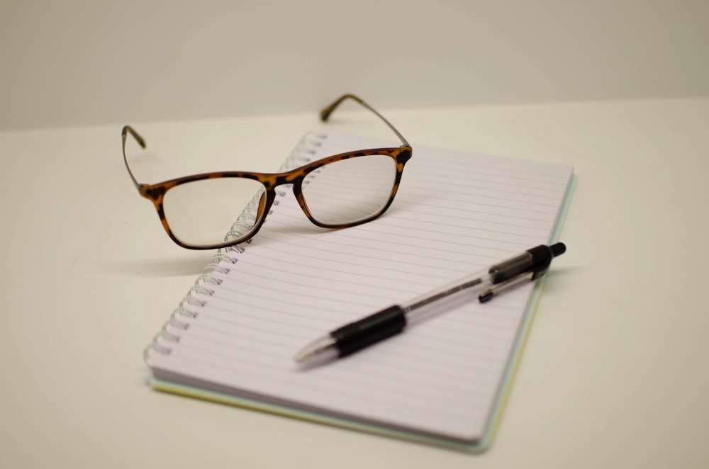 Reading glasses and a pen resting on a notepad.